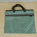 A green patterned document bag with black and gold striped handles and two zippers, resting flat on a light wooden surface.