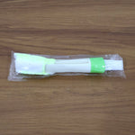 A white and green 3-in-1 cleaning brush sealed in clear plastic packaging on a wooden surface.