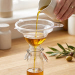 Funnel pouring oil into bottles in kitchen setting