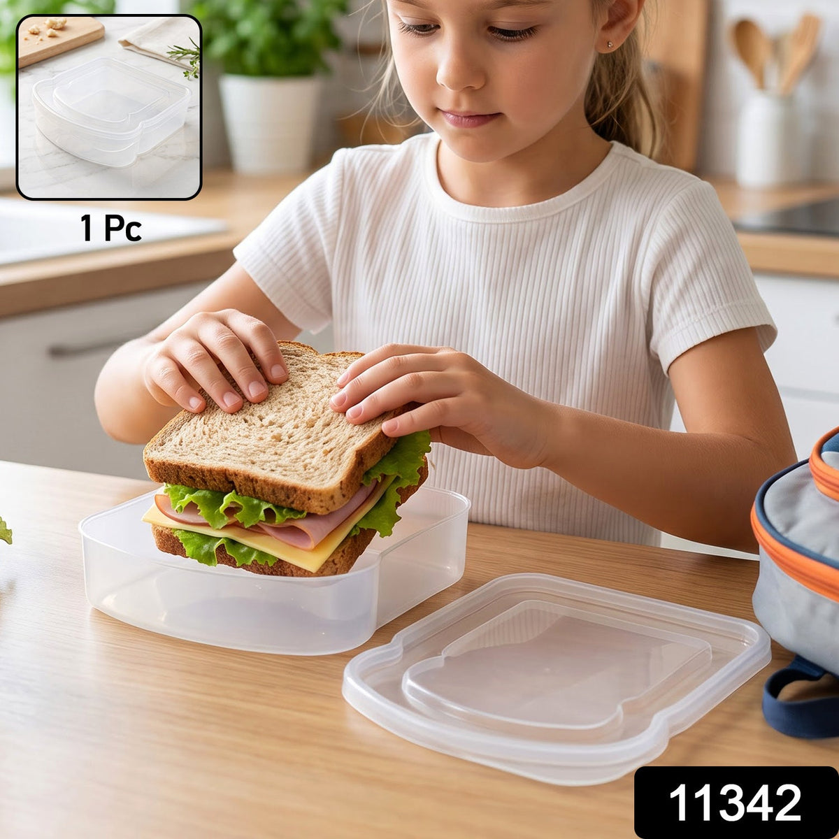 A clear plastic sandwich container with a lid rests on a marble surface with herbs and a cutting board in the background.