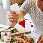A person drizzles oil from a clear plastic squeeze bottle with a red cap onto salmon and asparagus. – view 8