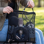 A person holds a black mesh zipper bag filled with microphones and audio cables outdoors, with a small inset of the empty