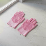 A pair of pink silicone scrubber gloves lying on a light-colored tiled floor near a window.