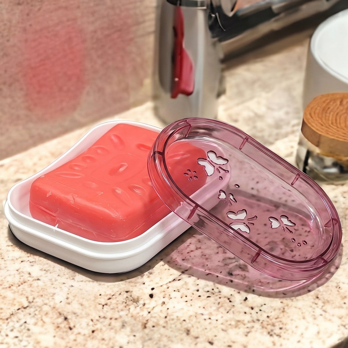 Pink bar of soap in a white base with a pink butterfly-patterned lid beside it on a marble counter.