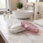 White bar of soap resting in a white base with a pink butterfly-patterned lid beside it on a marble counter in a bathroom.