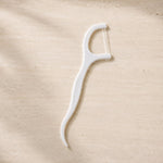 A single white dental floss pick with a textured handle lies on a light brown, textured surface.