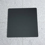 A square mirror with rounded corners lies flat on a speckled gray and white tiled floor.
