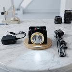 A black and gold headlamp with a solar panel, a charger, and a black and white head strap on a marble table.