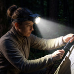 A woman wearing a black and gold headlamp with a bright beam, setting up a tent in a dark forest.