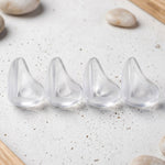 Four clear, rounded silicone corner protectors are lined up on a speckled white surface with light pebbles.