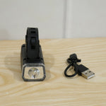 Black rectangular bicycle headlight with a clear lens and a USB charging cable resting on a light wooden surface.