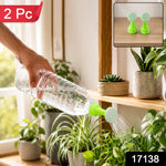 A hand holds a clear plastic bottle with a green and white sprinkler nozzle, watering indoor plants. A 2 Pc label is in the