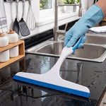 A gloved hand uses a white and blue squeegee to wipe water from a black kitchen countertop with a sink.