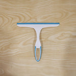 A white and blue squeegee lies flat on a light wooden surface with a visible grain.