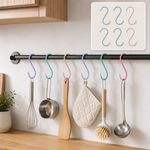 Six colorful plastic coated S hooks hanging kitchen utensils on a black rod in a modern kitchen.