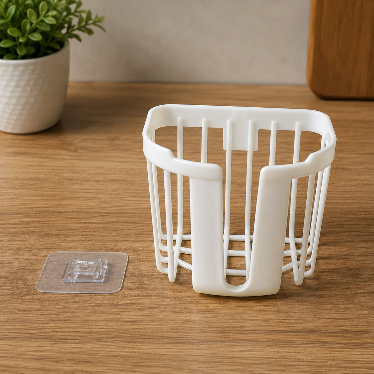 A white plastic toilet paper holder sits on a wooden surface next to a clear adhesive hook and a small green plant.
