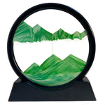 A black-framed circular sand art display with green sand forming two sets of mountains, on a white background.