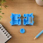 The light blue train-shaped pencil sharpener is open, revealing two sharpening blades and a small blue cap on a wooden desk.
