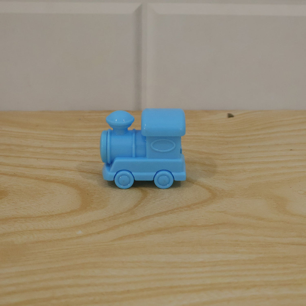 A light blue plastic train-shaped pencil sharpener resting on a light brown wooden surface with a white tiled background.