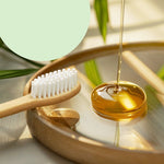 Close-up of a bamboo toothbrush with white bristles next to a wooden tray with a clear liquid being poured into a small dish.