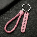 A close-up of a pink braided wrist loop keychain with a pink number tag on a black textured surface.