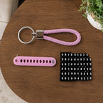 A pink braided wrist loop keychain, a pink number tag, and a sheet of number stickers on a wooden table.