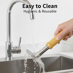 A hand holds the masher under running water from a chrome kitchen faucet, rinsing the perforated steel head in a sink.