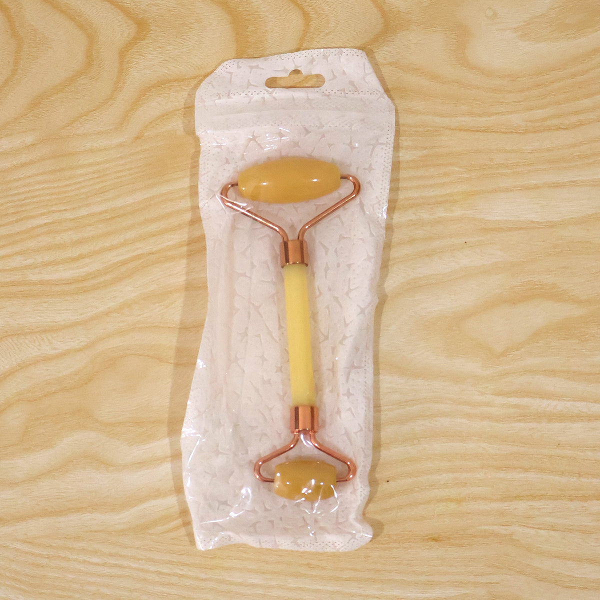 Dual-ended yellow jade facial roller in its clear plastic packaging