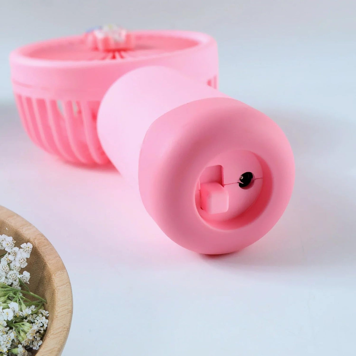 A pink bunny ear mini handheld fan stands on a desk next to books and a pen, with its USB charging cable visible.
