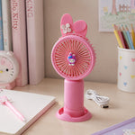 A pink bunny ear mini handheld fan with a small character on the grill stands upright, with its USB cable on a white