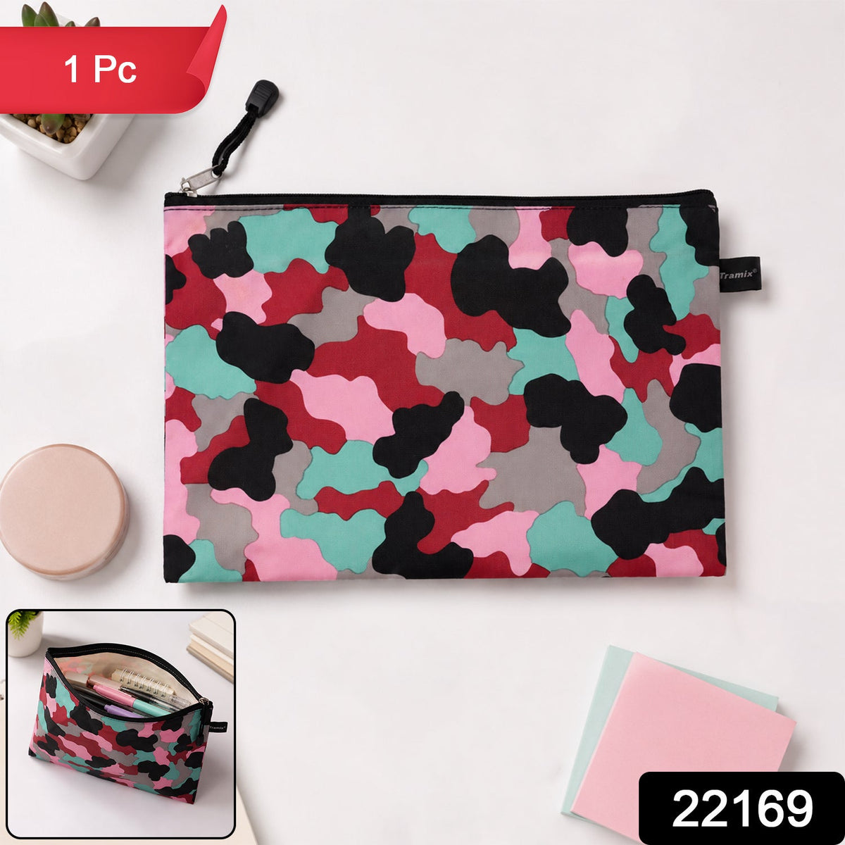 A flat, closed pouch with a pink, red, black, grey, and teal camouflage pattern, lying on a white surface next to a – view 2