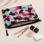 An open pouch with a pink, red, black, grey, and teal camouflage pattern, revealing its interior and surrounded by makeup