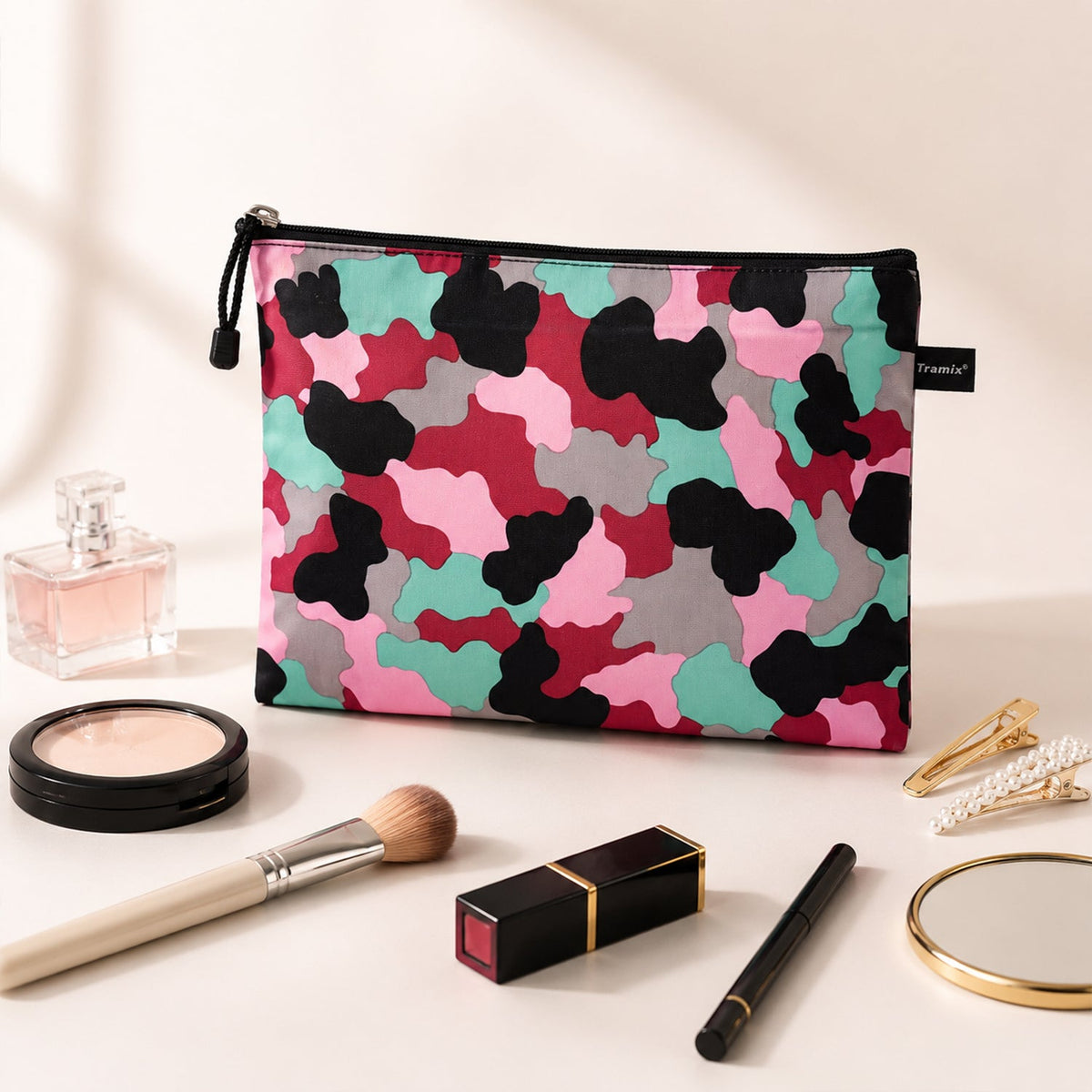 A pink, red, black, grey, and teal camouflage pattern pouch, surrounded by various makeup items like perfume, powder, a