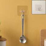 A silver spoon hanging from a transparent self-adhesive hook on a yellow wall, with a close-up inset.