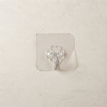 A transparent self-adhesive hook with a silver metal hook centered on a light beige tiled wall.
