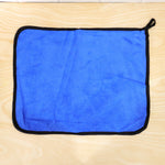 A blue microfiber cleaning cloth with a black border lies flat on a light wooden surface.