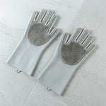 A pair of grey silicone scrubbing gloves with textured palms lays flat on a light grey tiled surface.