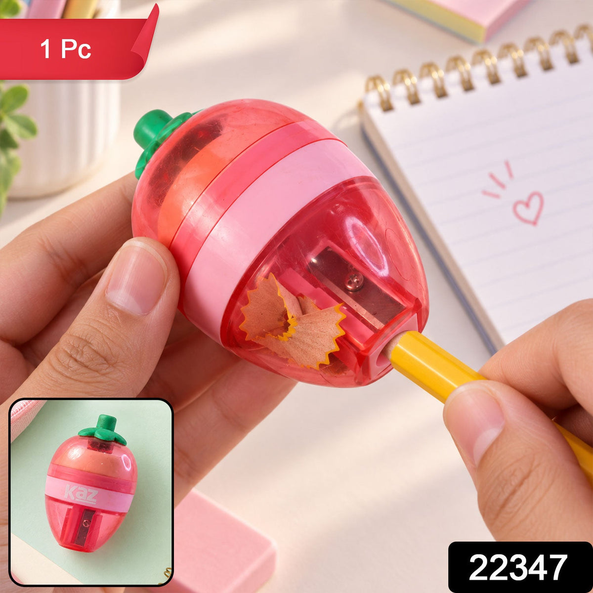 A pink and red strawberry-shaped sharpener with a green stem is held, showing a yellow pencil being sharpened.