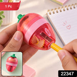 A pink and red strawberry-shaped sharpener with a green stem is held, showing a yellow pencil being sharpened.