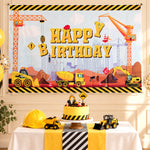 A construction-themed happy birthday banner hangs above a table with a cake, toy trucks, and a yellow hard hat.