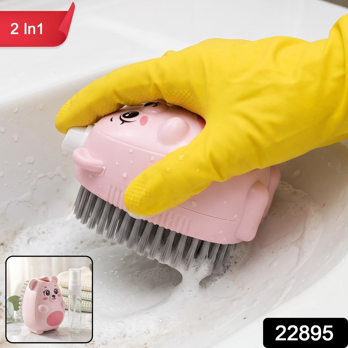A pink bear-shaped soap dispensing brush with grey bristles is held by a yellow-gloved hand, cleaning a sink.