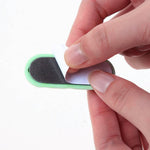 Hands peel the adhesive backing off a green silicone cable organizer.