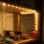 The illuminated LED strip lights provide ambient lighting for a collection of miniature cars in a wooden display case.