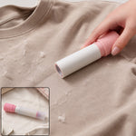 A hand uses a pink and white lint roller on a beige t-shirt covered in lint, with a smaller inset showing the roller.