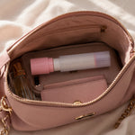 A pink and white lint roller, phone, perfume, and wallet are neatly packed inside an open pink handbag.