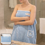 Woman wearing a light blue wearable bath towel with a white trim and a small pocket, standing in a bathroom.