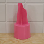 A pink plastic ground stake cup holder on a light wooden surface, with a white tiled wall in the background.