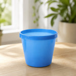 A single blue plastic planter pot sits on a light wooden surface in a bright room.