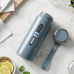 A blue insulated bottle with a detached cap and strap rests on a marble surface next to lemon slices and mint leaves.