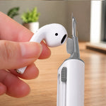 A hand holding a white earbud while the cleaning pen's small brush cleans the earbud speaker.